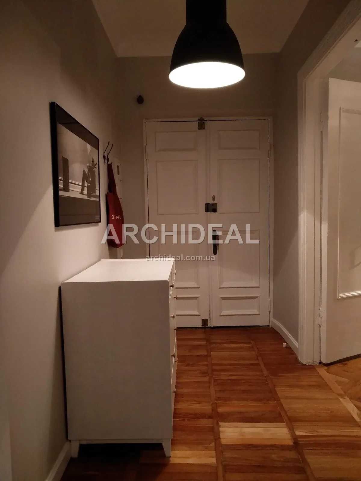 Двостулкові білі двері, комод, підвісний світильник